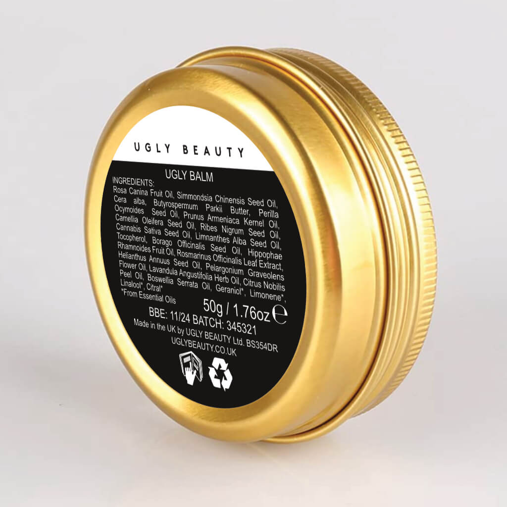 The underneath side of the Ugly Balm by "Ugly Beauty". The balm is a gold aluminium tin with a white and black label on the back.