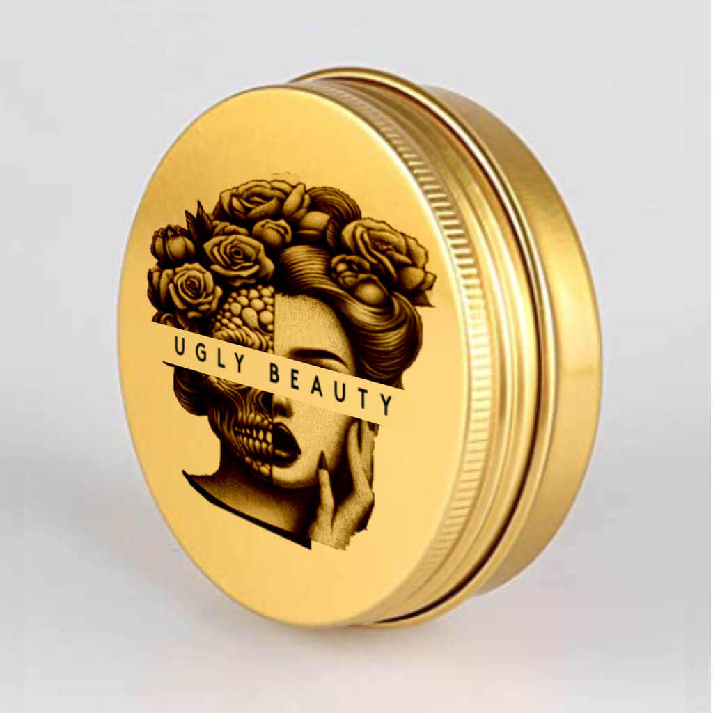 The front of the Ugly Balm by "Ugly Beauty". The balm is in a gold aluminium tin with the "Ugly Beauty" logo covering the eyes of a woman who is half monster or "Ugly" and half beautiful.